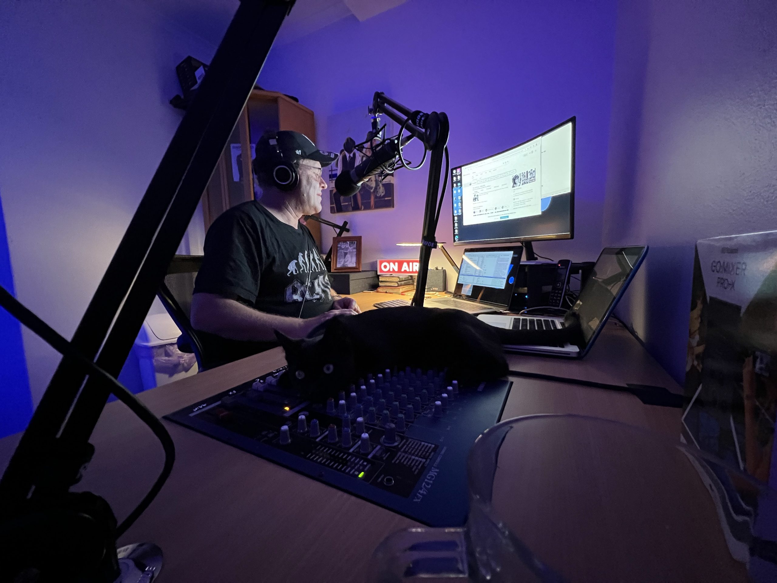 Paul Rothapfel sits at his desk in his studio. A cat is laying on the audio mixer controls.