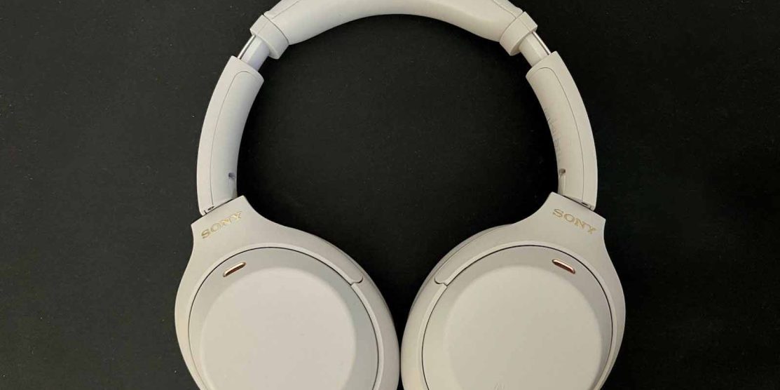 Picture shows Silver Sony headphones on a black flat background. The headphone cups are facing down.