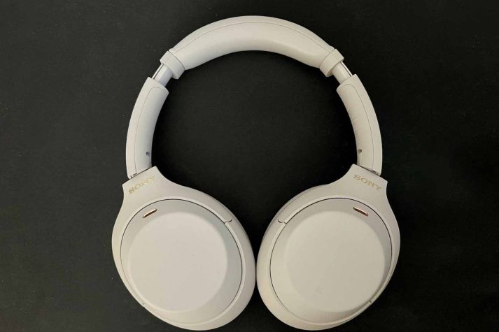 Picture shows Silver Sony headphones on a black flat background. The headphone cups are facing down.