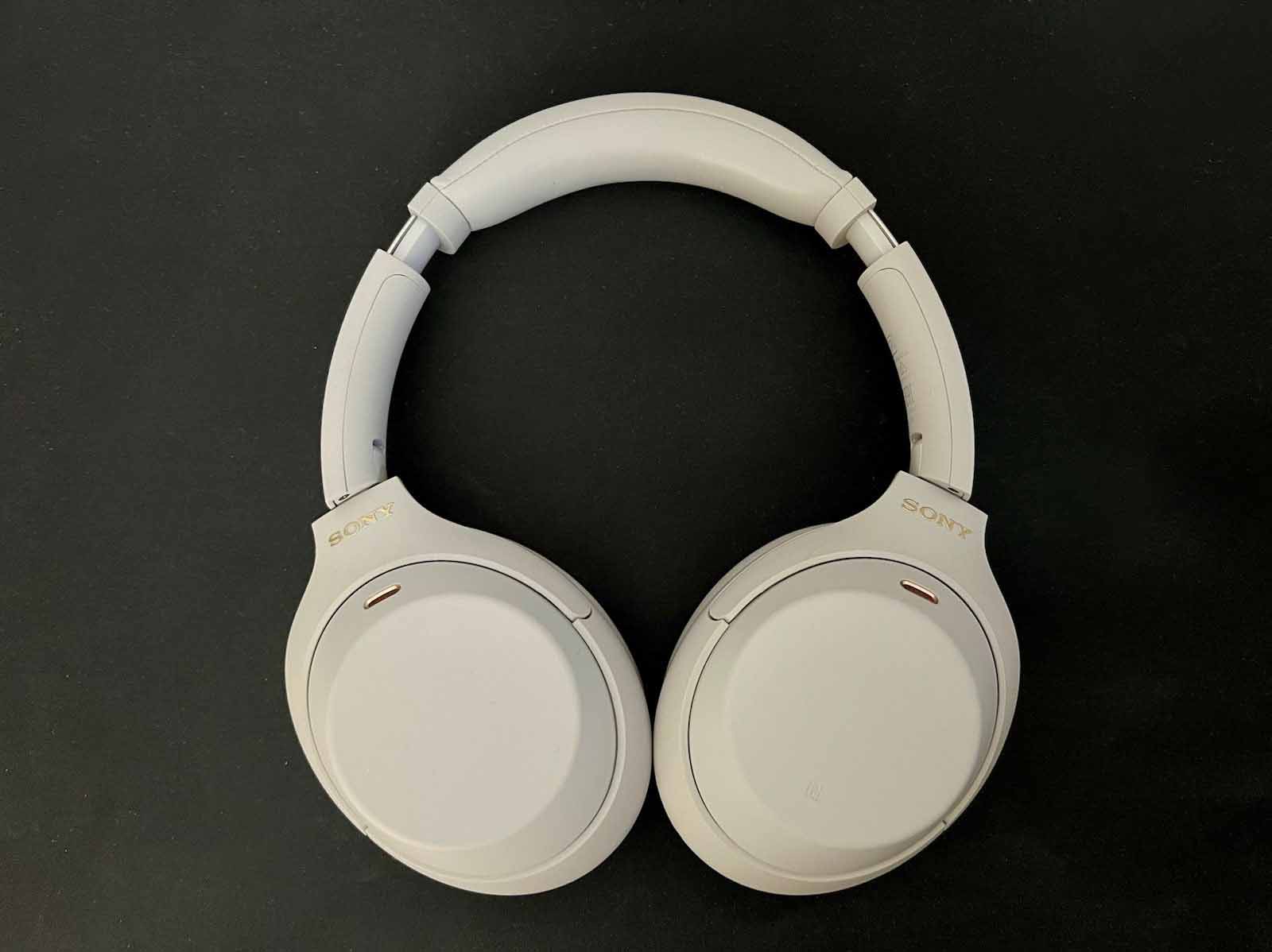 Picture shows Silver Sony headphones on a black flat background. The headphone cups are facing down.