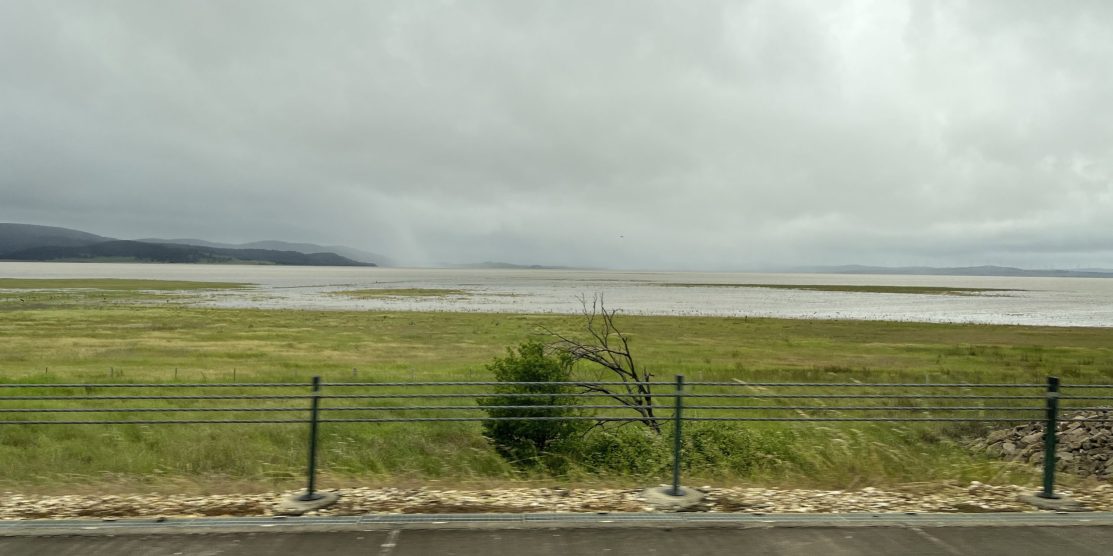 Picture shows grey sky and Lake George full of water from the roadside.