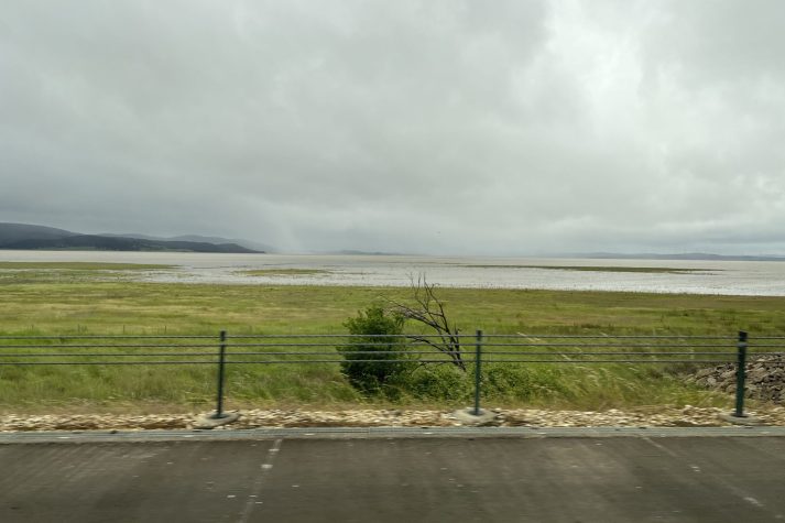 Picture shows grey sky and Lake George full of water from the roadside.