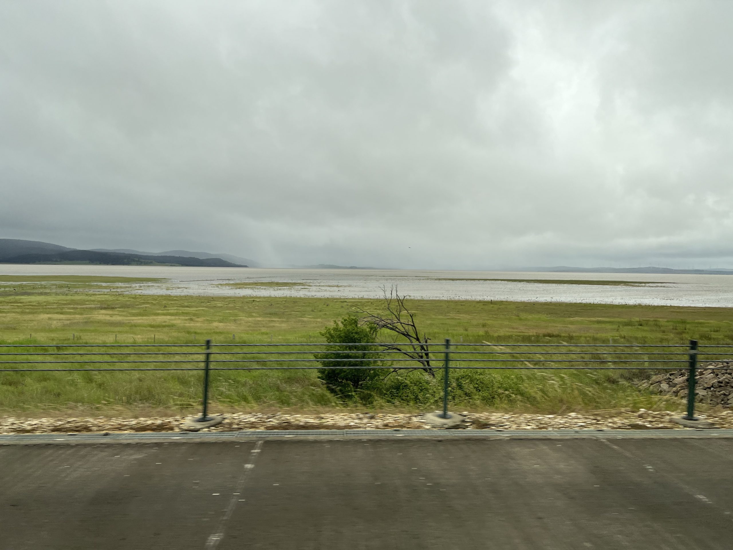 Picture shows grey sky and Lake George full of water from the roadside.